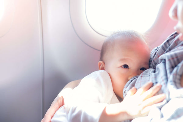 Infant nursing on airplane by window demonstrating feeding during flight for pressure relief and comfort with babies