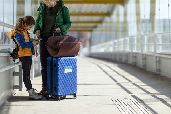 Parent and young child in yellow vest with blue rolling suitcase at bright train station preparing for family travel journey