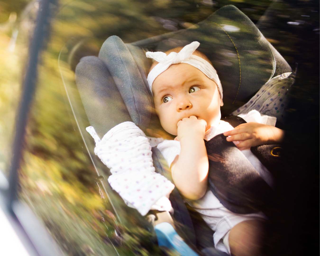 Baby secured in car seat looking up during family road trip with natural sunlight