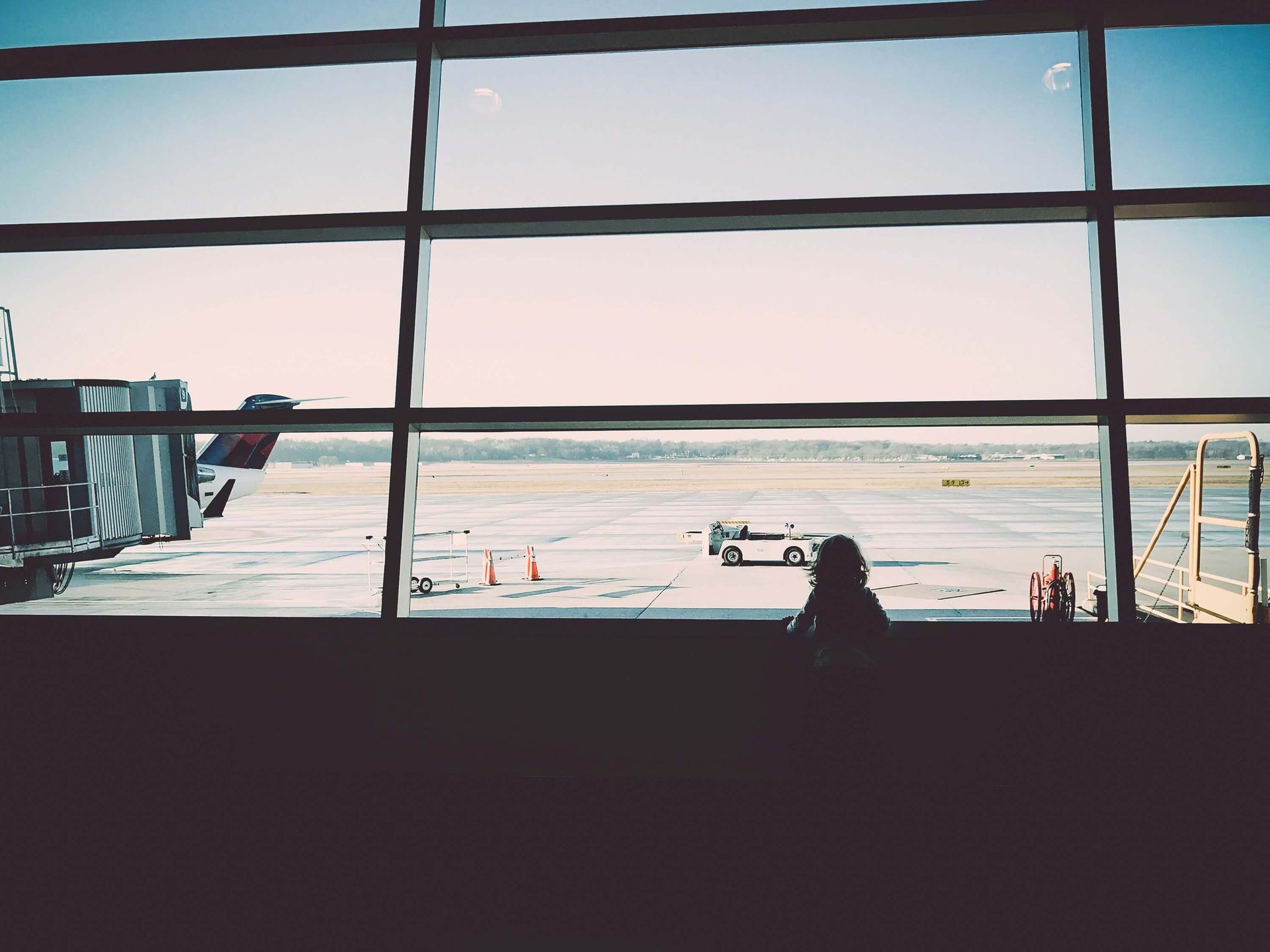 Silhouette of child looking out large airport terminal window at tarmac and airplane showing travel anticipation and wonder