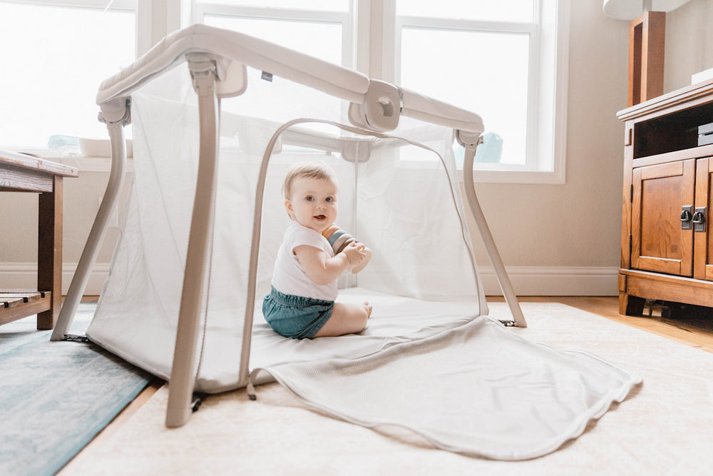 Baby sitting inside Chicco Alfa Lite travel playard with mesh sides in bright kitchen