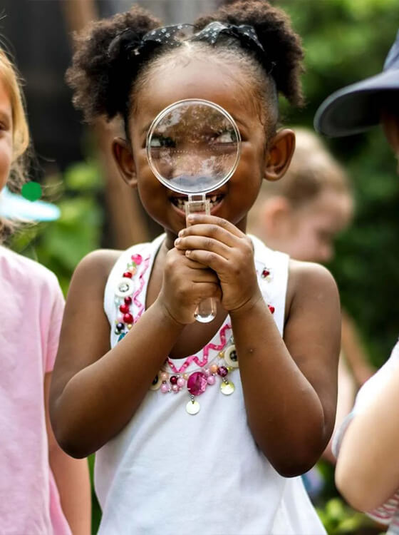 Three children holding colorful magnifying glasses outdoors exploring and discovering nature together