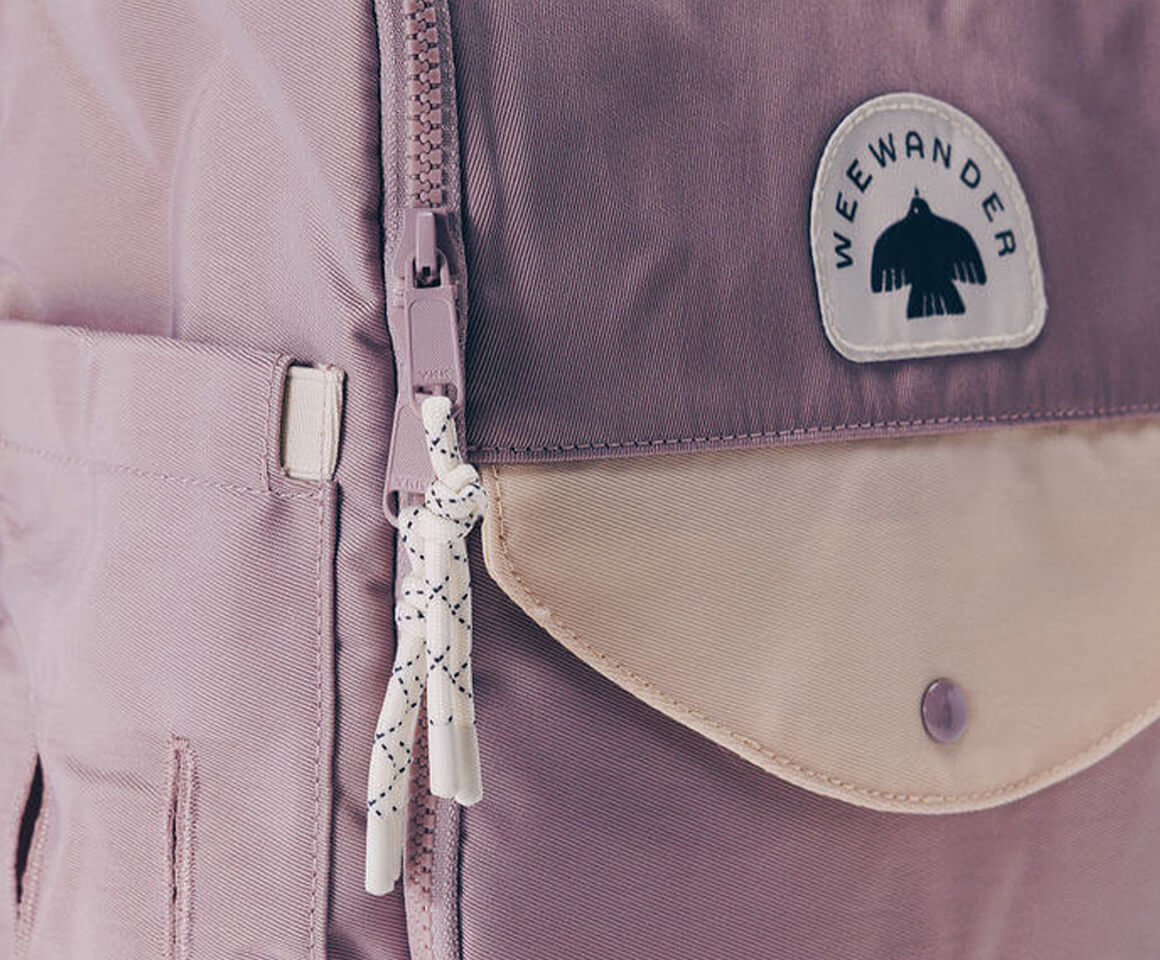 Close-up of WeeWander purple backpack showing logo badge cream envelope pocket and chunky zipper pull